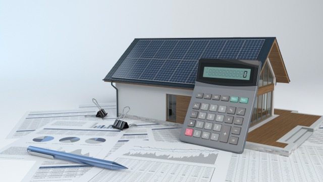 Hausmodell mit Solarpanelen neben Taschenrechner und Diagrammen